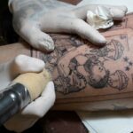 Argentine tattooist Tebi Cobra Vucinovich works on a tattoo of Argentina's forward Lionel Messi kissing the FIFA World Cup trophy on the leg of Ariel Sacchi at Ds Tattoo Shop in Buenos Aires on December 23, 2022 (Photo by JUAN MABROMATA / AFP)