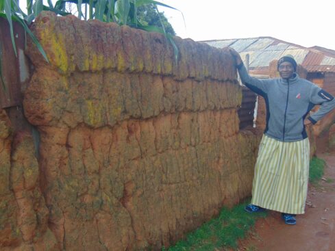 wakilin kaka stands by an earlier type of wall made from red sand, but not using blocks